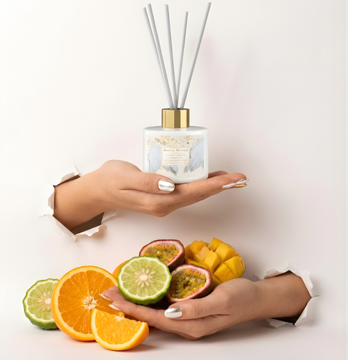 Eleganter Angel Wings Raumduft-Diffuser in cleanem Weiß mit silbernen Stäbchen im Torn-Paper-Look. Hände präsentieren den Flakon zusammen mit frischen Orangenscheiben, Bergamotte, Mango und Passionsfrucht durch weißes, gerissenes Papier – Best Bougie sanfter Premium Wohnduft.
