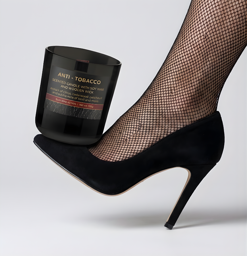 Funktionale schwarze Anti-Tobacco Wood Duftkerze mit Holzdocht, kunstvoll balanciert auf der Spitze eines eleganten schwarzen High-Heels mit Netzstrumpfhose vor hellem Hintergrund – Best Bougie Lifestyle-Deko.