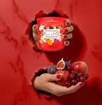 Romantische Duftkerze Flower & Heart in leuchtendem Rot im Torn-Paper-Look. Hände präsentieren die Kerze zusammen mit frischen Feigen, roten Äpfeln und Kirschen durch rotes, gerissenes Papier – Best Bougie fruchtiger Premium Raumduft.