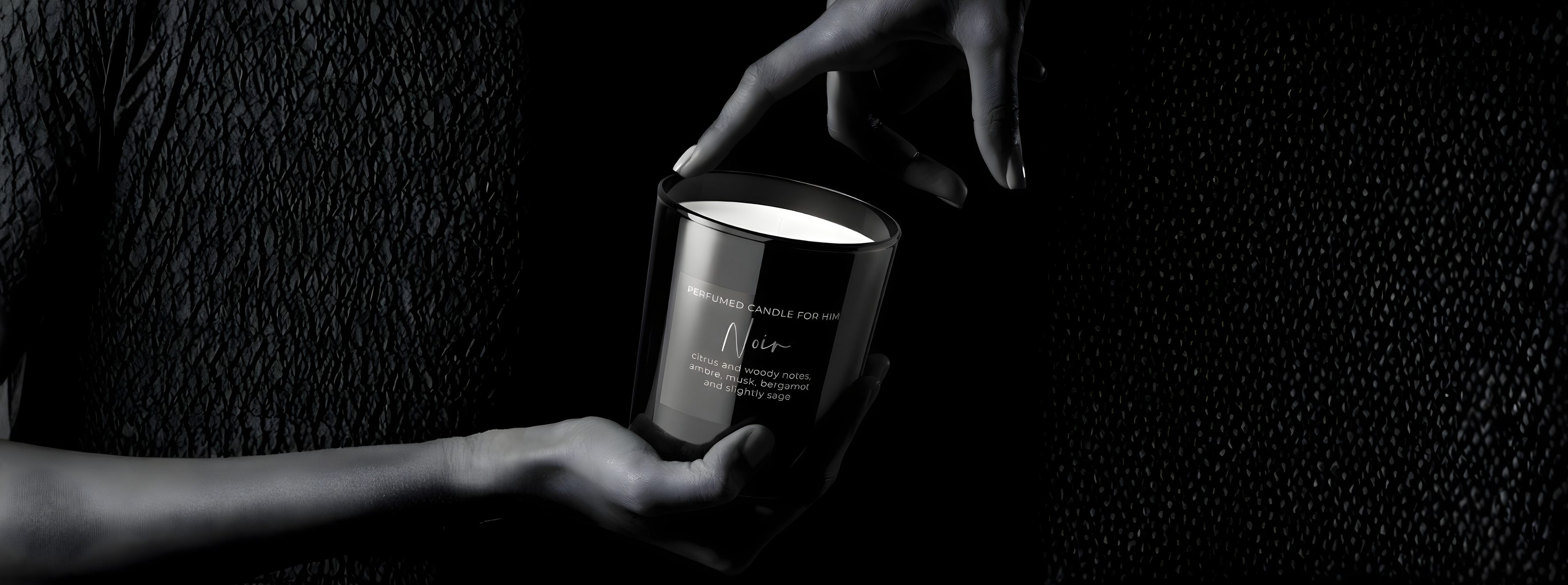 Edle schwarze Noir Duftkerze „For Him“ in einer dramatischen Low-Key-Aufnahme. Eine Hand hält das glänzende Glas, während eine zweite Hand die Kerze sanft berührt – Best Bougie maskuliner Premium Raumduft mit Zitrus- und Holznoten.