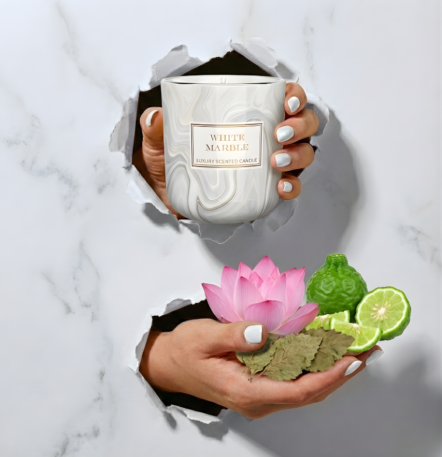 Elegante Duftkerze White Marble in weißer Marmor-Optik im Torn-Paper-Look. Hände präsentieren die Kerze zusammen mit einer pinken Lotusblüte, frischen Bergamotte-Stücken und getrockneten Blättern durch weißes, gerissenes Papier – Best Bougie Luxus-Raumduft.