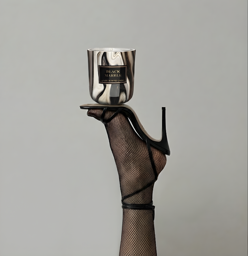 Exklusive Duftkerze Black Marble in Marmor-Optik, kunstvoll balanciert auf der Sohle eines eleganten schwarzen Riemchen-High-Heels mit Netzstrumpfhose vor grauem Hintergrund – Best Bougie Luxus-Raumduft.