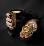 Exklusive schwarze Duftkerze Noir für Männer im Torn-Paper-Look. Hände präsentieren die brennende Kerze zusammen mit Bergamotte, Salbei und Ambra-Harz durch schwarzes, gerissenes Papier – Best Bougie maskuliner Luxus-Raumduft.