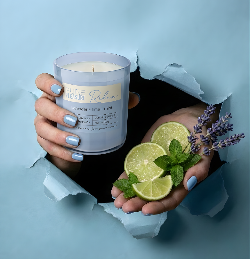 Kreative Inszenierung der hochwertigen Duftkerze Pure Pleasure Relax. Hände ragen durch hellblaues, gerissenes Papier und präsentieren die Kerze zusammen mit frischen Limetten, Minze und Lavendel – Best Bougie entspannender Raumduft