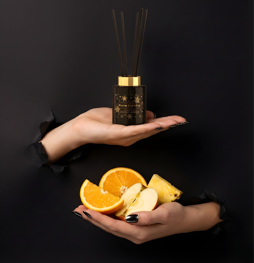Eleganter Warm Evening Raumduft-Diffuser in edlem Schwarz mit Golddekor und schwarzen Stäbchen im Torn-Paper-Look. Hände präsentieren den Flakon zusammen mit frischen Orangenscheiben, einem Apfelstück und Ananas durch schwarzes, gerissenes Papier – Best Bougie luxuriöser Wohnduft.